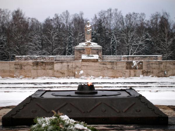 Brāļu kapu siena ar mātes Latvijas tēlu centrā. Priekšplānā - mūžīgā uguns. Avots: https://lv.wikipedia.org/wiki/R%C4%ABgas_Br%C4%81%C4%BCu_kapi#/media/Att%C4%93ls:M%C5%AB%C5%BE%C4%ABg%C4%81_uguns_Br%C4%81%C4%BCu_kapos.JPG