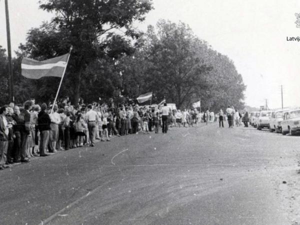 Akcijas “Baltijas ceļš “ dalībnieki pie Iecavas ar sarkanbaltsarkaniem karogiem. Bauskas rajons, pie Iecavas, 1989. gada 23. augusts. Autors: V. Koršunovs. Latvijas Nacionālā arhīva Latvijas Valsts kinofotofonodokumentu arhīvs, 1. f., 141921N.l.