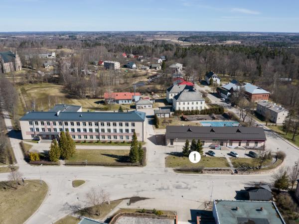 1. attēls. Cesvaines kroga ēkas atlikusī daļa (1) ar tajā ierīkoto veikalu “Lats”. Cesvaine, Rīgas iela 2. Aizmugurējā plānā pa kreisi – Cesvaines baznīca. 2022.g. 17.aprīlis. V.Grīviņa foto.